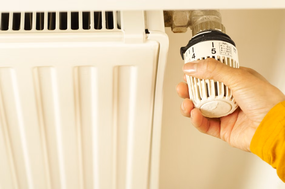 Close-up of hand adjusting radiator thermostat to control home heating temperature.